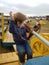 Toddler boy in blue sweater with dirty pants  playing on farm equipment with rusted wheel.