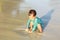 Toddler boy in blue swimsuit playing in shallow water on beach