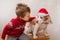 Toddler boy in Christmas jacket holding beagle in Santa hat