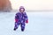 Toddler boy dressing warm winter snowsuit walking on snow field at cold season