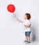 Toddler boy or girl in white t-shirt, shoes, denim shorts. Child smiling, holding red balloon, posing sideways isolated on white