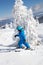 Toddler boy in helmet, goggles and blue overalls skiing in beautiful snowy mountains