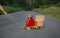 Toddler boy in red overalls sits on a big toy car - a truck with cardboard boxes, talking on phone