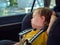 Toddler boy sleeps peacefully and safe while secured with seat belts in the car