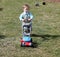 Toddler boy in a suit pushing a lawn mower