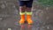 Toddler child in orange boots walks through the puddles after the rain. Closeup