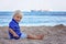 Toddler child, sitting on beach, watching lighted ship in the ocean