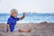 Toddler child, sitting on beach, watching lighted ship in the ocean