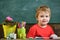 Toddler cute and cheerful ready to study. Kid boy in classroom near flower in pot and pencils, chalkboard on background