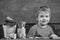 Toddler cute and cheerful ready to study. Kid boy in classroom near flower in pot and pencils, chalkboard on background