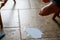 toddler foot suspended above spilled milk, crumbs, and a plastic fork on a brown tile floor