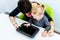 Toddler girl in child occupational therapy session doing sensory playful exercises with her therapist using digital tablet.