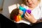 Toddler girl with popit toy in rainbow colours. Dino shape silicone toy for stress relief. Bubbles sensory trendy fidget