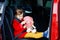 Toddler girl sitting in car seat, holding plush soft doll toy and looking out of the window on nature and traffic