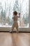 Toddler girl standing up against dirty window looking out