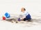 Toddler with Hat & Sunglasses Plays on a Sandy Beach Building Sand Castles