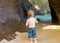 A toddler inspecting a cave at a beach in the caribbean