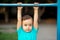 Toddler kid learning to do pull ups exercise at gym lesson in kindergarten: preschooler hanging on steel bar at sports ground