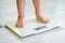 Toddler legs on white scale at home. Bare feet on a weight scale. Measuring and controlling baby weight