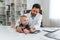 Toddler is lying down on the table. Doctor with little baby is working in the cabinet