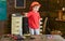 Toddler in protective hard hat, helmet at home in workshop. Child cute and adorable playing with tools, as builder or