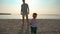 Toddler runs across the sand near the ocean to the camera smiling and waving.