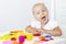 Toddler sculpts from colored plasticine on a white table.