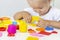 Toddler sculpts from colored plasticine on a white table.