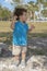 A toddler stands upon a large rock at the park,looks to his left.