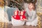 Toddler twins in red reindeer santa claus costumes are sitting at home with their mother against background of christmas tree