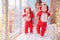 Toddler twins in red reindeer santa claus costumes are sitting at home with their mother against background of window with
