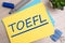 toefl. text on yellow paper on light wooden background with stationery