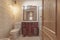 Toilet with reddish-colored wooden cabinet with square mirror