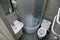 Toilet room interior with white toilet bowl, shower cabin and grey wall tiles