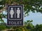 toilet sign board hanging on green leaves tree at the public outdoor park.