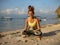 Tolasana, Scale Pose. Seated lifted arm balance. Attractive woman practicing yoga on the beach. Ocean view. Legs in Lotus pose.
