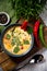 Tom yum soup portion on a wooden board and table. Slightly above view. Decorated with hot pepper and herb leaves. Green table