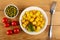 Tomato, bowl with green peas, plate with cubes of fried potatoes, fork on wooden table. Top view