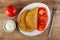 Tomato, bowl with mayonnaise, dish with two fried cheburek, slices of tomato, fork on table. Top view