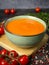 Tomato cream soup in a green bowl on a wooden board. Cherry tomatoes, pink pepper, salt, herbs around the bowl