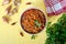 Tomato lobio of green bean pods in a bowl on a bright yellow background. Flat lay, top view