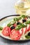 Tomato and mozzarella caprese salad and pesto sauce with olives on gray table