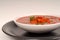 Tomato, red pepper, basil soup in white bowl with light gray background