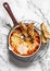 Tomato sauce beans, cheese, eggs baked shakshuka in a ceramic frying pan with a grill crispy bread on a light background, top view