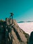 Toned image adult man with backpack stands on the edge of a cliff and looks into the distance against the blue sky