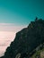 Toned image adult woman with a backpack stands on the edge of a cliff and looking at the sunrise against the blue sky