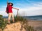 Toned image of a little boy with a backpack and a hat that holds the stick and standing on a sandy hill and smiling against the ba