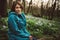 Toned photo of happy hiking middle-aged woman in blue jacket sitting and resting in evening spring forest