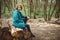 Toned photo of happy hiking middle-aged woman in blue jacket sitting and resting in evening spring forest