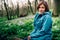 Toned photo of happy hiking middle-aged woman in blue jacket sitting and resting in evening spring forest